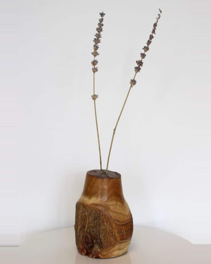 Hand-carved wooden vase with two dried lavender stems against a light background