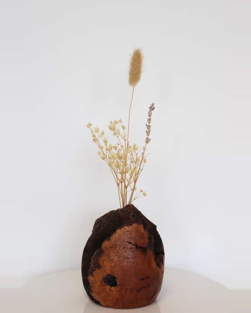 Dried floral arrangement in a round, burnt-orange ceramic vase on a white surface against a pale background.