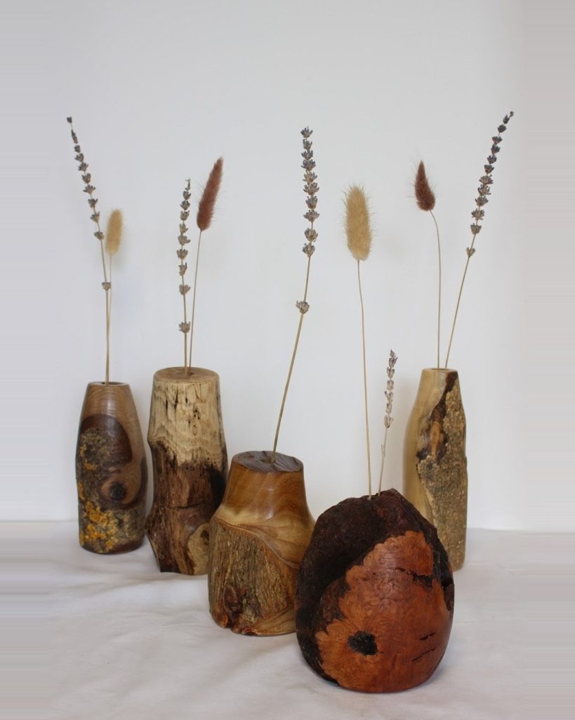 Wooden vases of varying shapes and sizes arranged on a white surface, each holding tall dried grasses and seedheads.